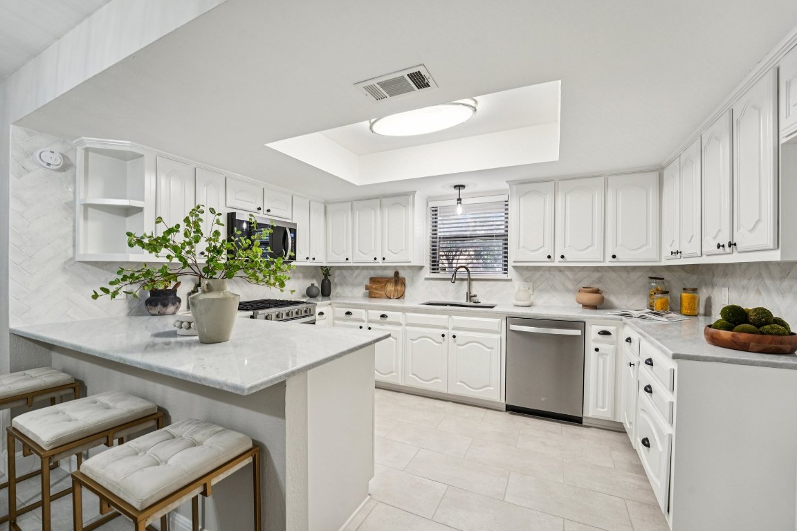 5307 Beckett Circle Austin, TX 78749 - Photo 11 of 29 Kitchen with a tray ceiling, open shelves, light stone countertops, a peninsula, and appliances with stainless steel finishes