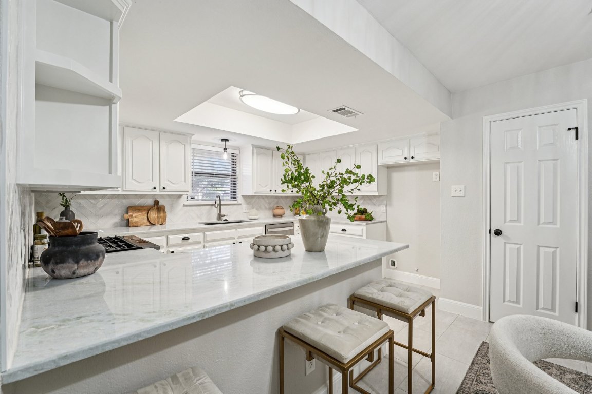 5307 Beckett Circle Austin, TX 78749 - Photo 12 of 29 Kitchen with a peninsula, light stone counters, a kitchen breakfast bar, and white cabinets