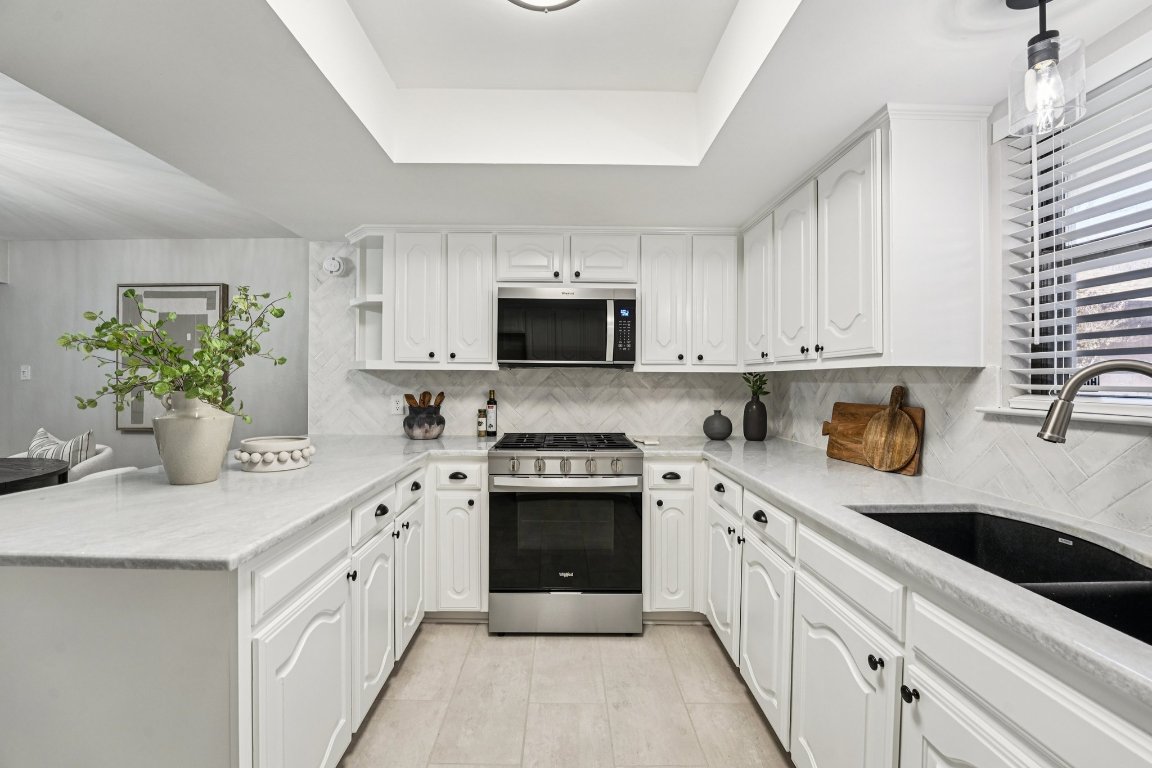 5307 Beckett Circle Austin, TX 78749 - Photo 13 of 29 Kitchen featuring stainless steel appliances, a tray ceiling, light stone countertops, decorative backsplash, and a peninsula
