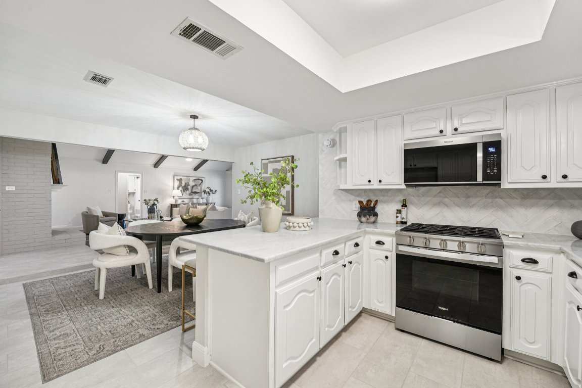 5307 Beckett Circle Austin, TX 78749 - Photo 15 of 29 Kitchen featuring appliances with stainless steel finishes, a peninsula, decorative backsplash, white cabinets, and light stone countertops