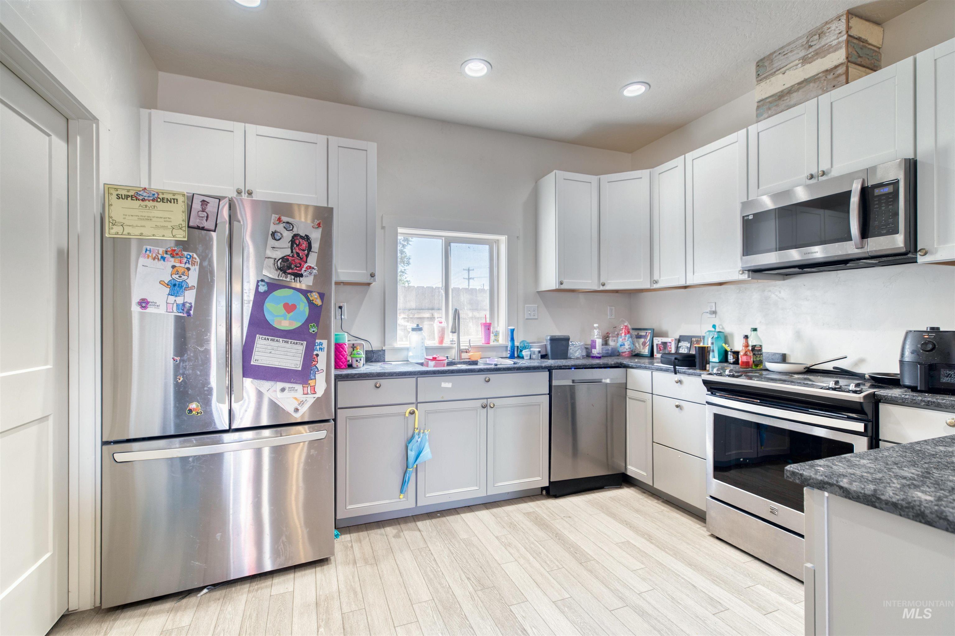 112 East Main Street Nyssa, OR 97913 - Photo 32 of 43 Kitchen featuring appliances with stainless steel finishes, dark countertops, light wood-style flooring, recessed lighting, and white cabinetry