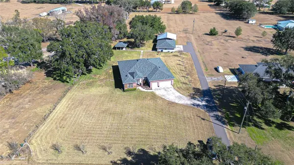 an aerial view of a house with backyard and trees all around
