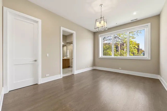 an empty room with wooden floor chandelier and windows