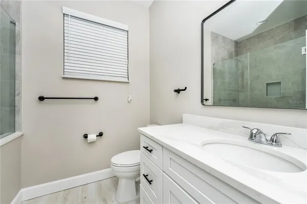 a bathroom with a granite countertop toilet a sink a mirror and a window