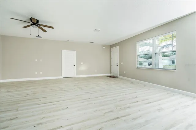 an empty room with wooden floor a ceiling fan and windows
