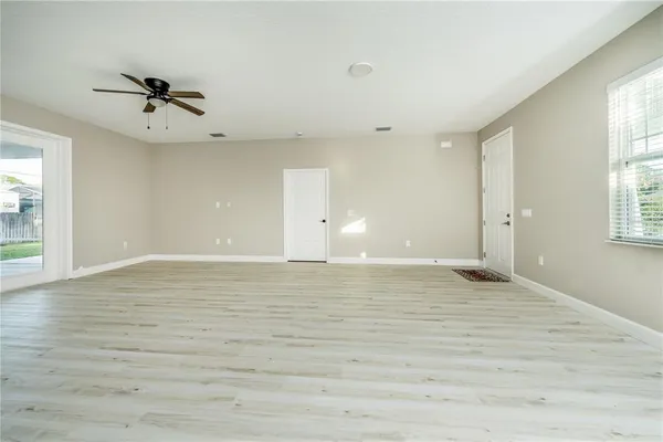 an empty room with wooden floor a ceiling fan and windows