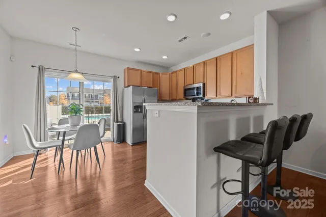 a kitchen with stainless steel appliances granite countertop a stove a refrigerator a microwave a dining table and chairs with wooden floor