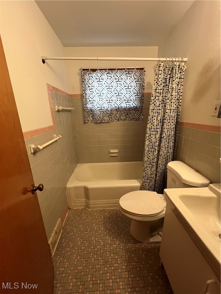 11406 Granger Road Cleveland, OH 44125 - Photo 8 of 28 Full bathroom featuring vanity, toilet, shower / bathtub combination with curtain, and tile walls