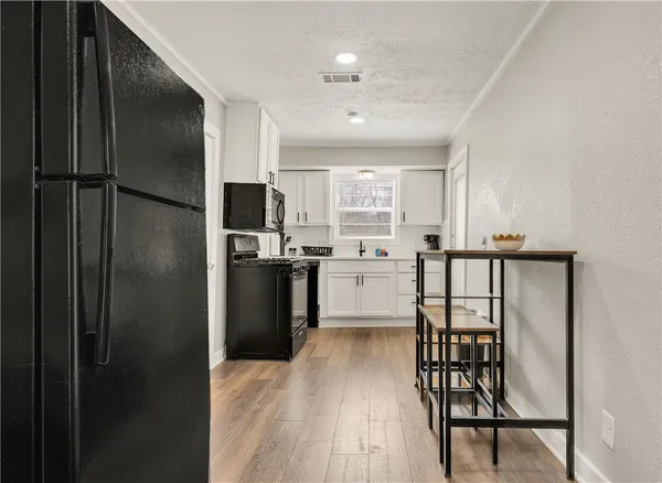 a kitchen with stainless steel appliances granite countertop a refrigerator a microwave oven a sink and white cabinets with wooden floor