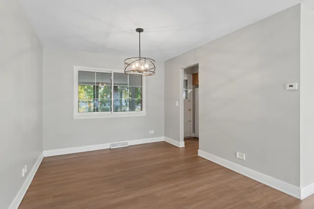 an empty room with wooden floor chandelier and window