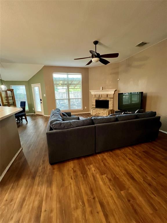 12201 Rolling Ridge Drive Fort Worth, TX 76028 - Photo 8 of 21 Spacious living area featuring wood-finish flooring, a brick fireplace with a decorative mantel, and a ceiling fan with integrated lighting