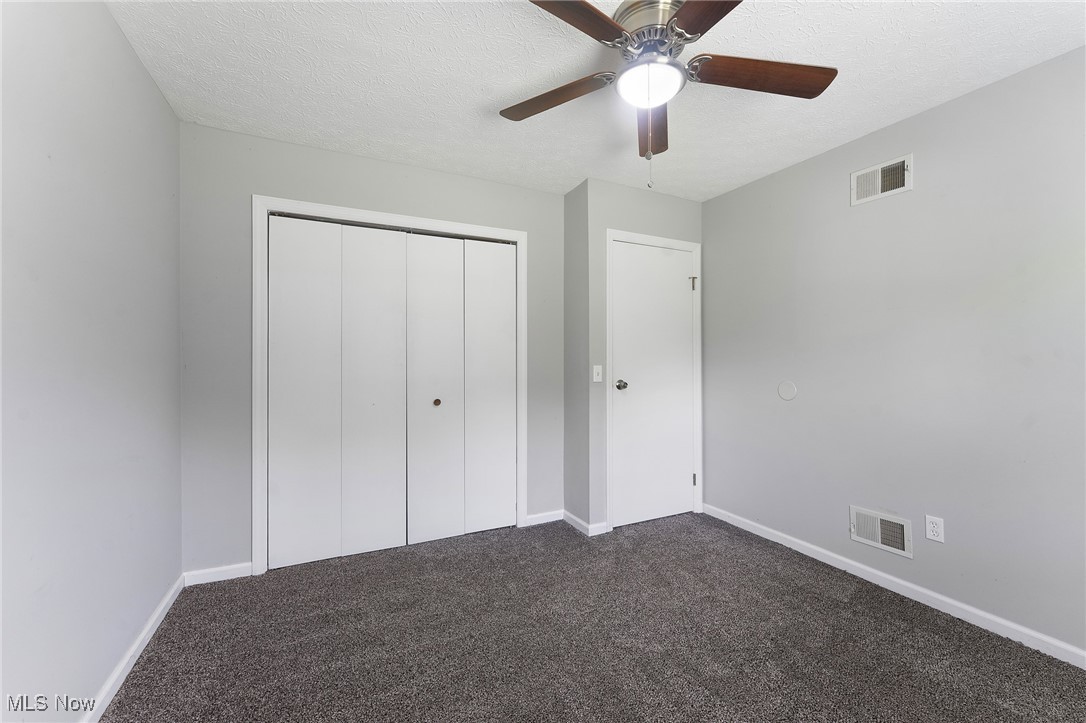 1761 Rustic Run Road Warren, OH 44481 - Photo 38 of 45 Unfurnished spare bedroom featuring dark carpet, a closet, a textured ceiling, and a ceiling fan