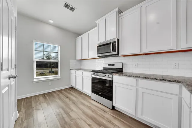 a kitchen with granite countertop white cabinets appliances a sink and a window
