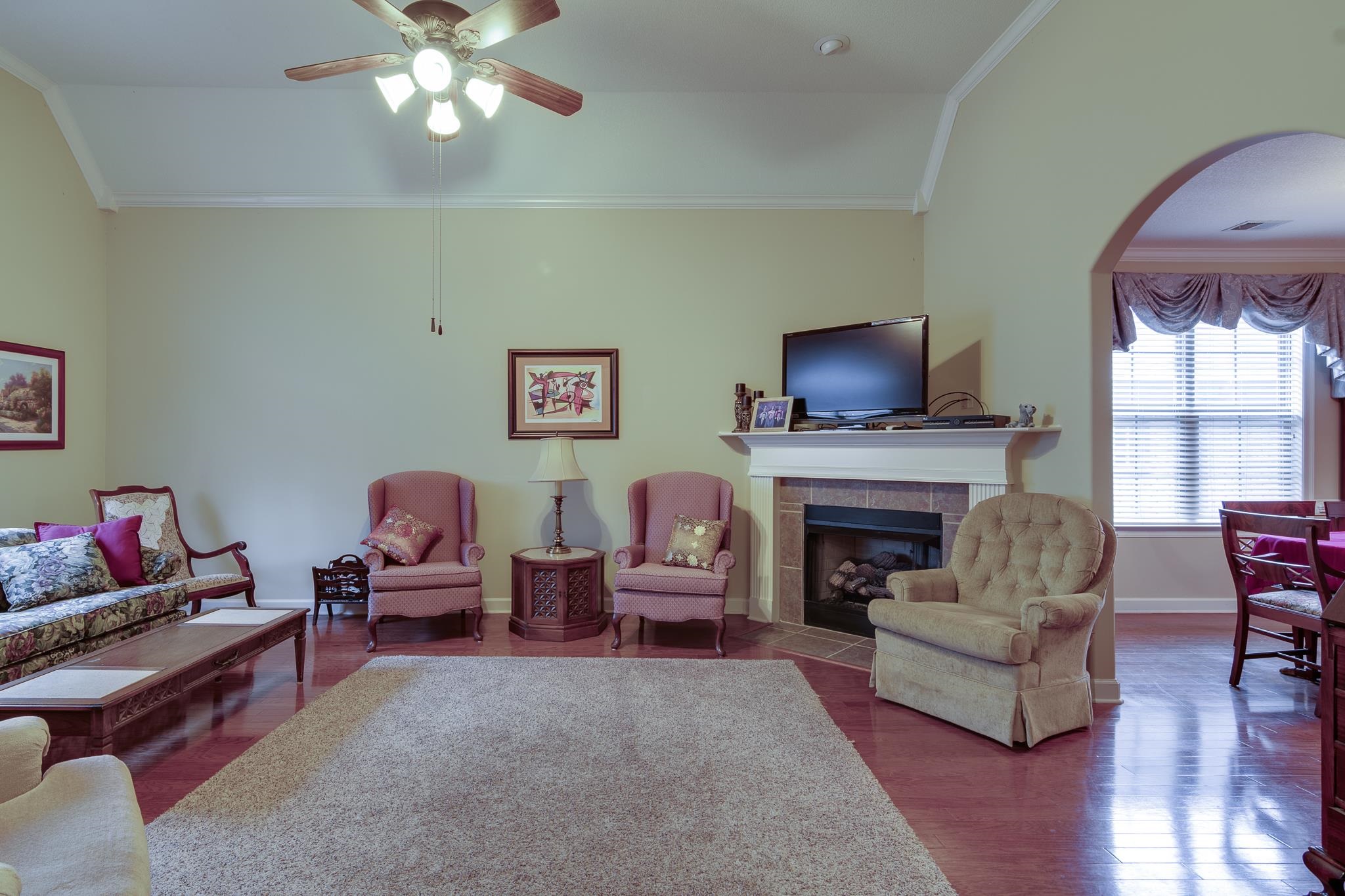 Living room featuring ceiling fan, hardwood / wood-style floors, vaulted ceiling, a fireplace, and ornamental molding