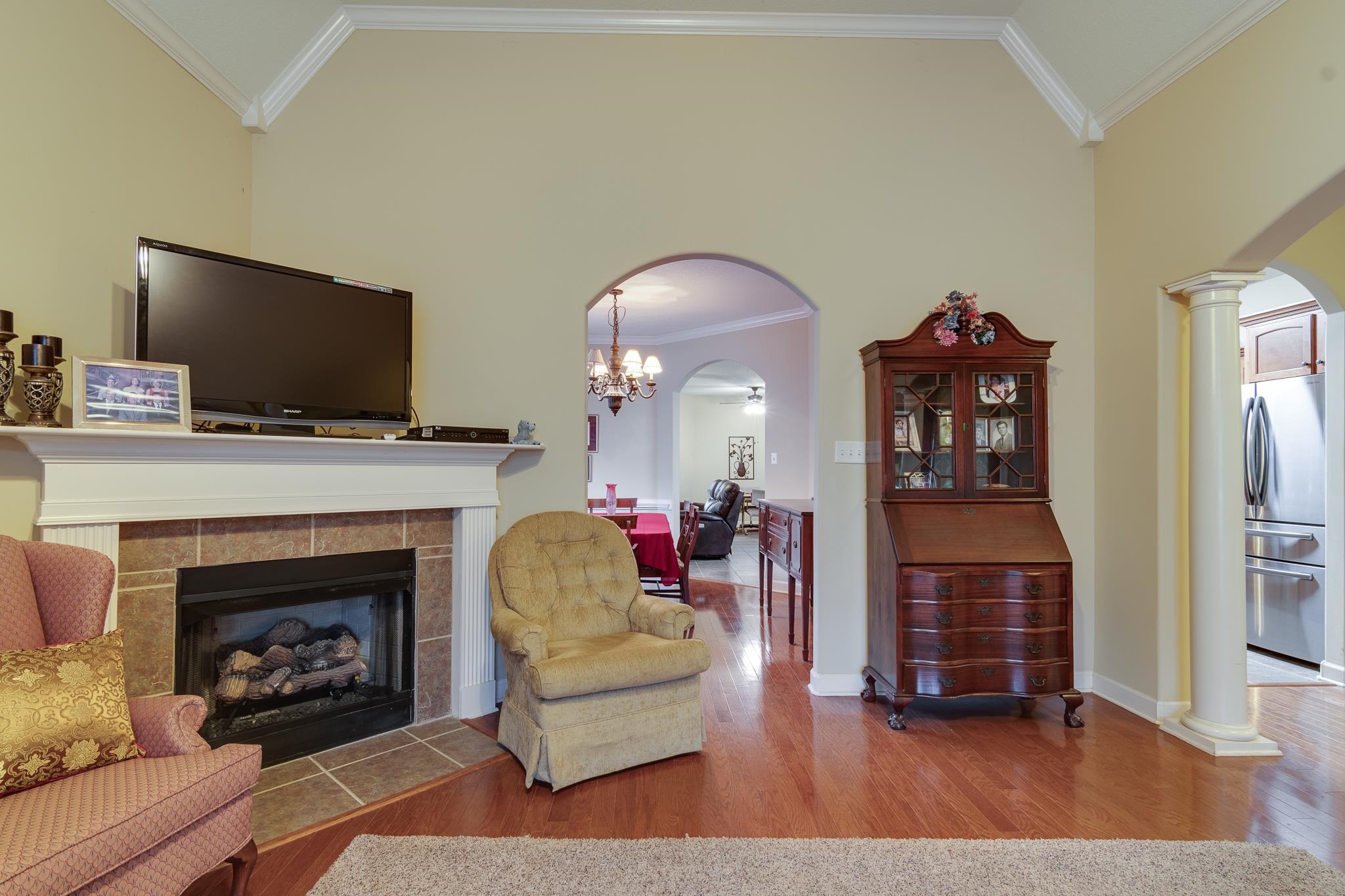 Living room with decorative columns, ornamental molding, a tile fireplace, hardwood / wood-style flooring, and high vaulted ceiling