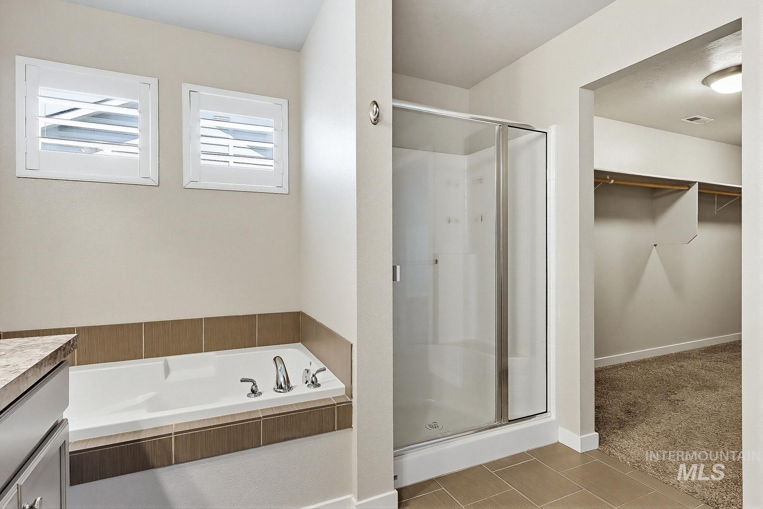 846 North Hidden View Way Star, ID 83669 - Photo 35 of 49 Bathroom featuring a built-in tub with tile surround, a glass-enclosed shower, dual windows with white plantation shutters, and large format floor tiling