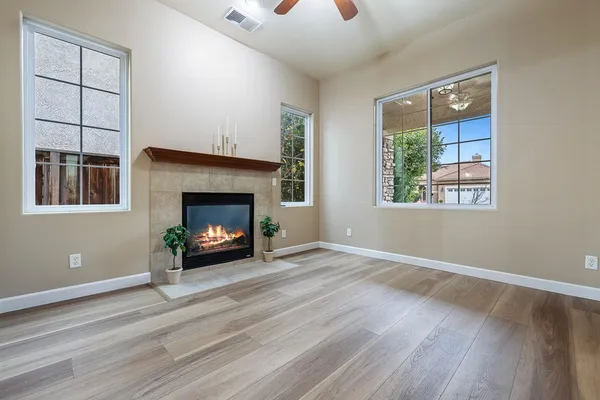 an empty room with wooden floor a ceiling fan a fireplace and windows