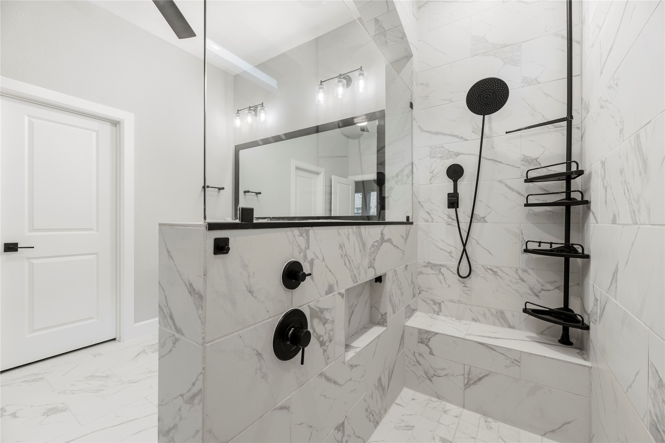 3438 Rich Radish Road Richmond, TX 77406 - Photo 11 of 25 Indulge in the luxury "super shower," designed with floor-to-ceiling marble-patterned wall tile, an integrated bench seat, a built-in product niche, and a 9-inch Moen Isabel rain showerhead in a matte black finish.