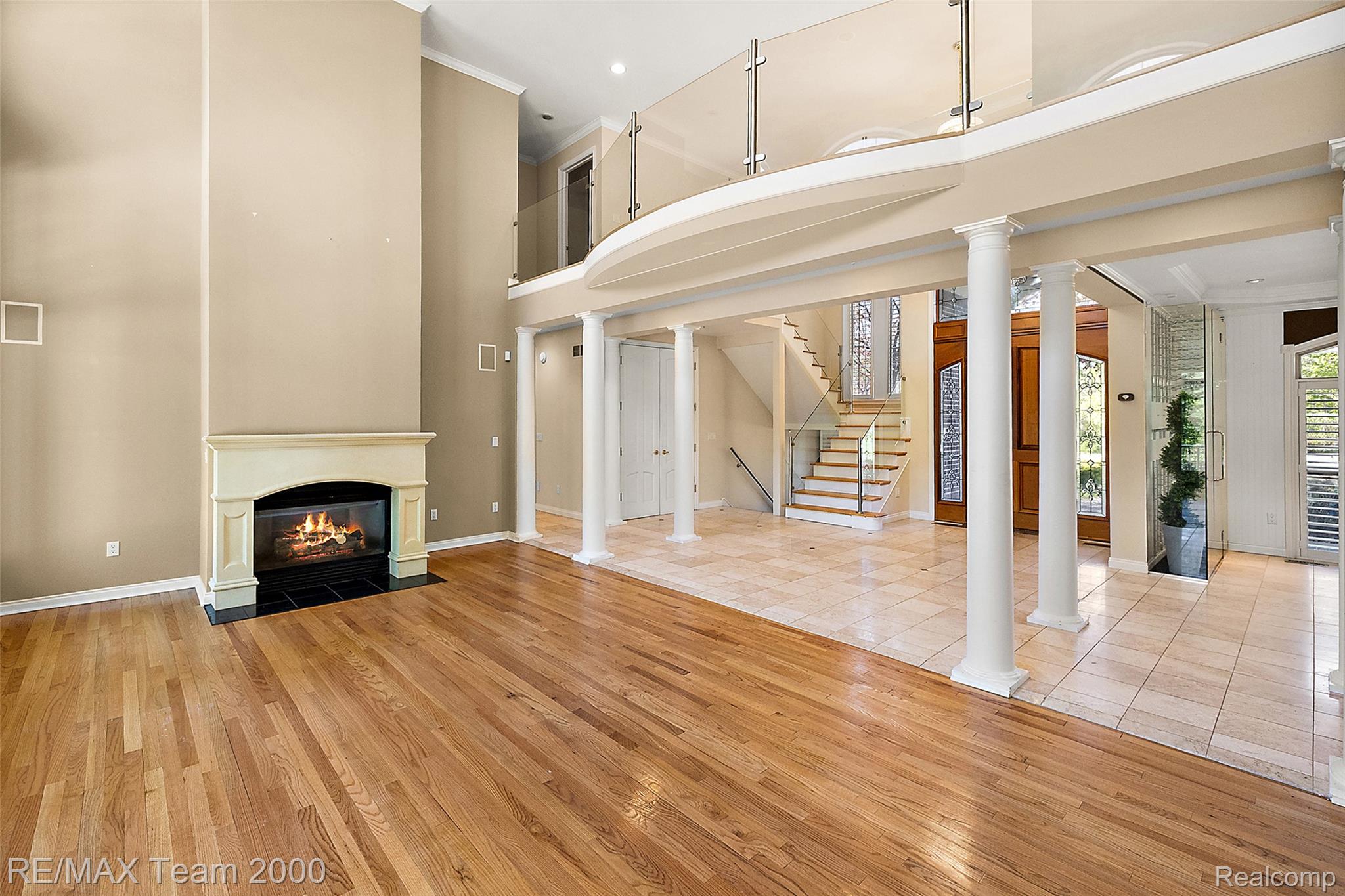 630 Sheldon Court Rochester, MI 48306 - Photo 19 of 94 Unfurnished living room featuring ornate columns, light wood-type flooring, a fireplace with flush hearth, a high ceiling, and crown molding