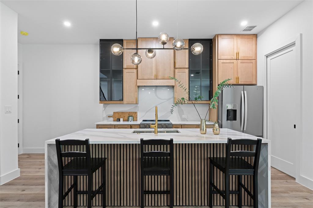 2828 Rochester Street Dallas, TX 75215 - Photo 8 of 36 Kitchen featuring a breakfast bar, light stone countertops, light wood-type flooring, stainless steel fridge with ice dispenser, and an island with sink
