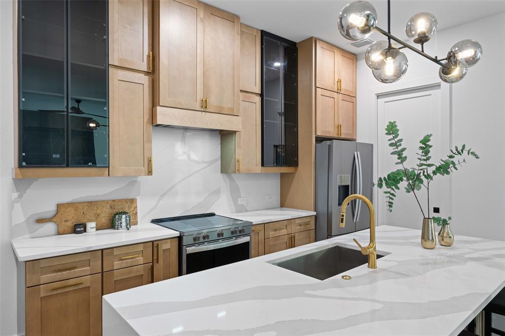 2828 Rochester Street Dallas, TX 75215 - Photo 9 of 36 Kitchen with glass insert cabinets, light stone counters, appliances with stainless steel finishes, a center island with sink, and pendant lighting