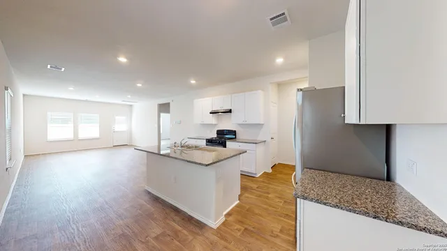 a kitchen with stainless steel appliances granite countertop a sink a stove a refrigerator and island with wooden floor