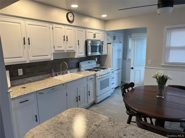 a large kitchen with stainless steel appliances a sink dishwasher a stove a refrigerator a microwave oven with white cabinets and wooden floor