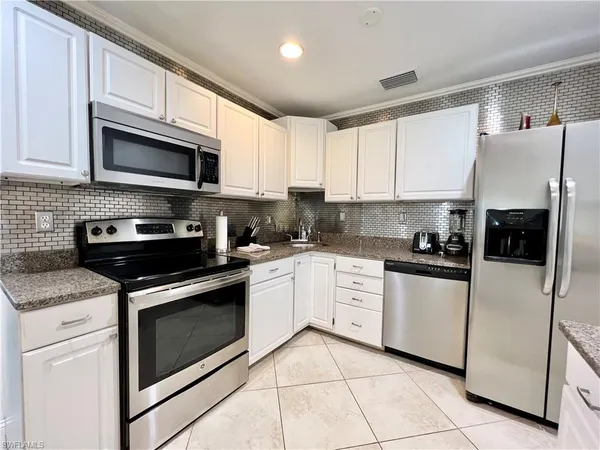 a kitchen with stainless steel appliances granite countertop grey cabinets a stove a sink and a microwave