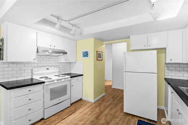 a kitchen with a refrigerator a stove a sink and white cabinets with wooden floor