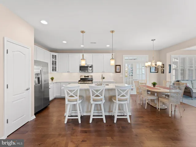a kitchen with stainless steel appliances kitchen island granite countertop a dining table chairs and white cabinets