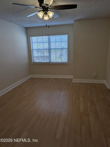 an empty room with wooden floor chandelier fan and windows