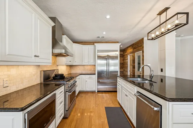 a kitchen with granite countertop a sink stainless steel appliances wooden floor and cabinets