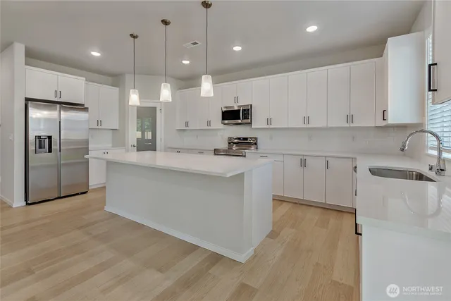 a kitchen with stainless steel appliances granite countertop a sink a stove a refrigerator and white cabinets