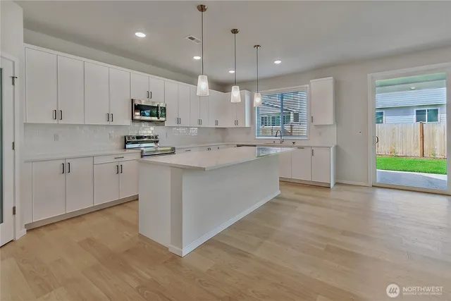 a kitchen with stainless steel appliances kitchen island granite countertop a stove a sink a refrigerator and white cabinets with wooden floor