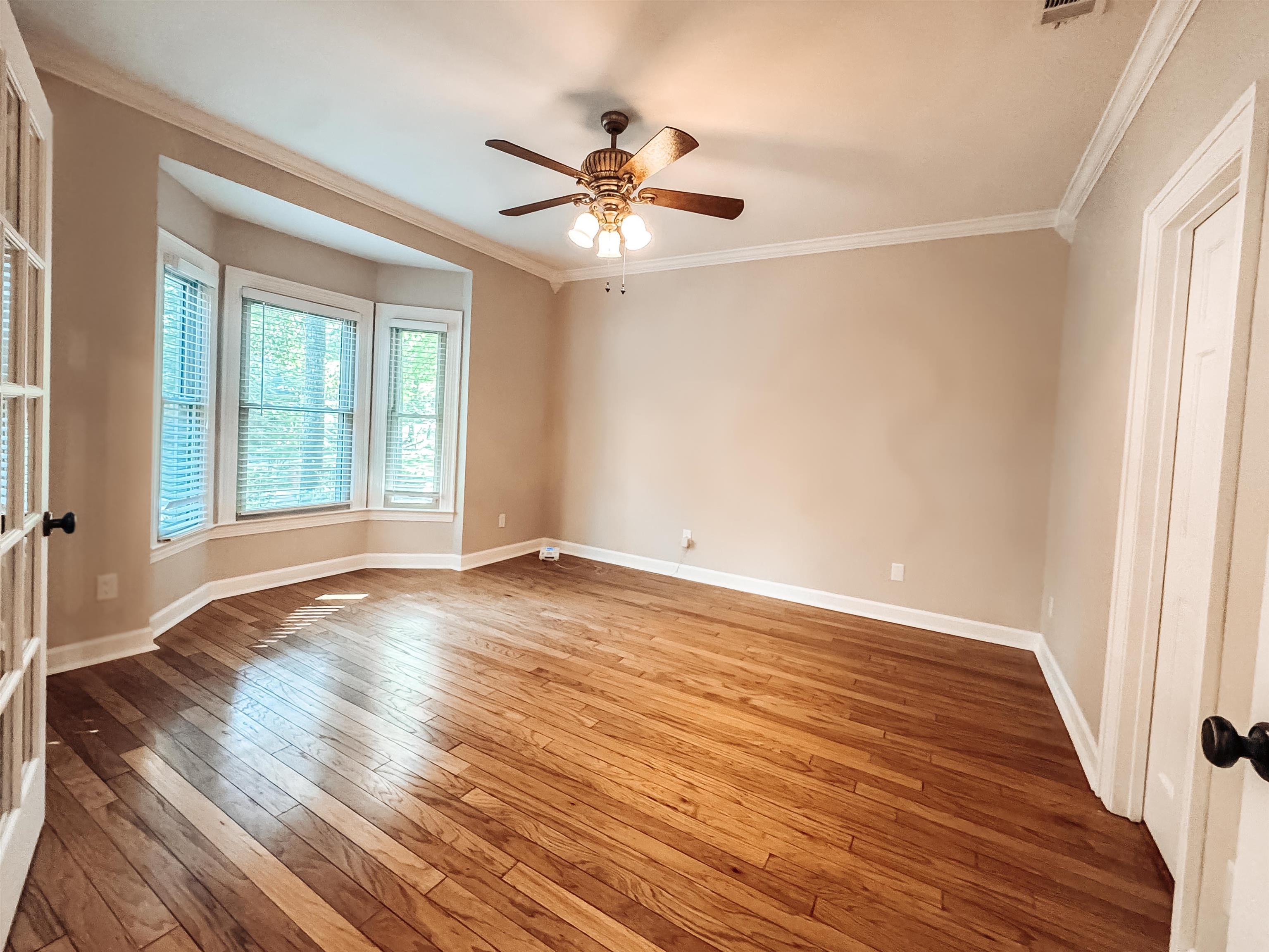 832 South Tree Drive Collierville, TN 38017 - Photo 9 of 40 Spacious room featuring wood-finish flooring, a bay window with blinds, crown molding, and a ceiling fan with light fixture