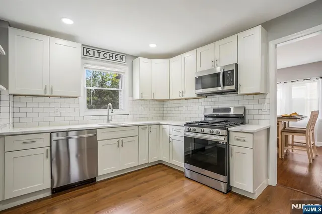 a kitchen with stainless steel appliances granite countertop a stove top oven a sink dishwasher a microwave oven and a refrigerator with wooden floors