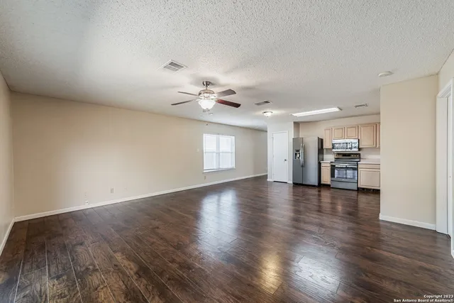 a view of empty room with wooden floor and kitchen