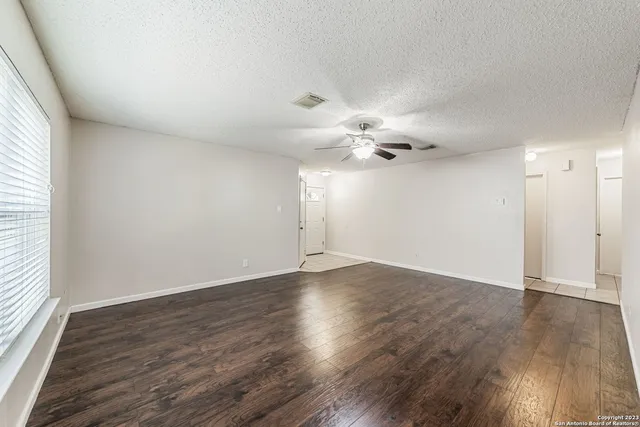 an empty room with wooden floor chandelier fan and windows
