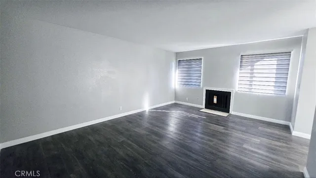 an empty room with wooden floor fireplace and windows