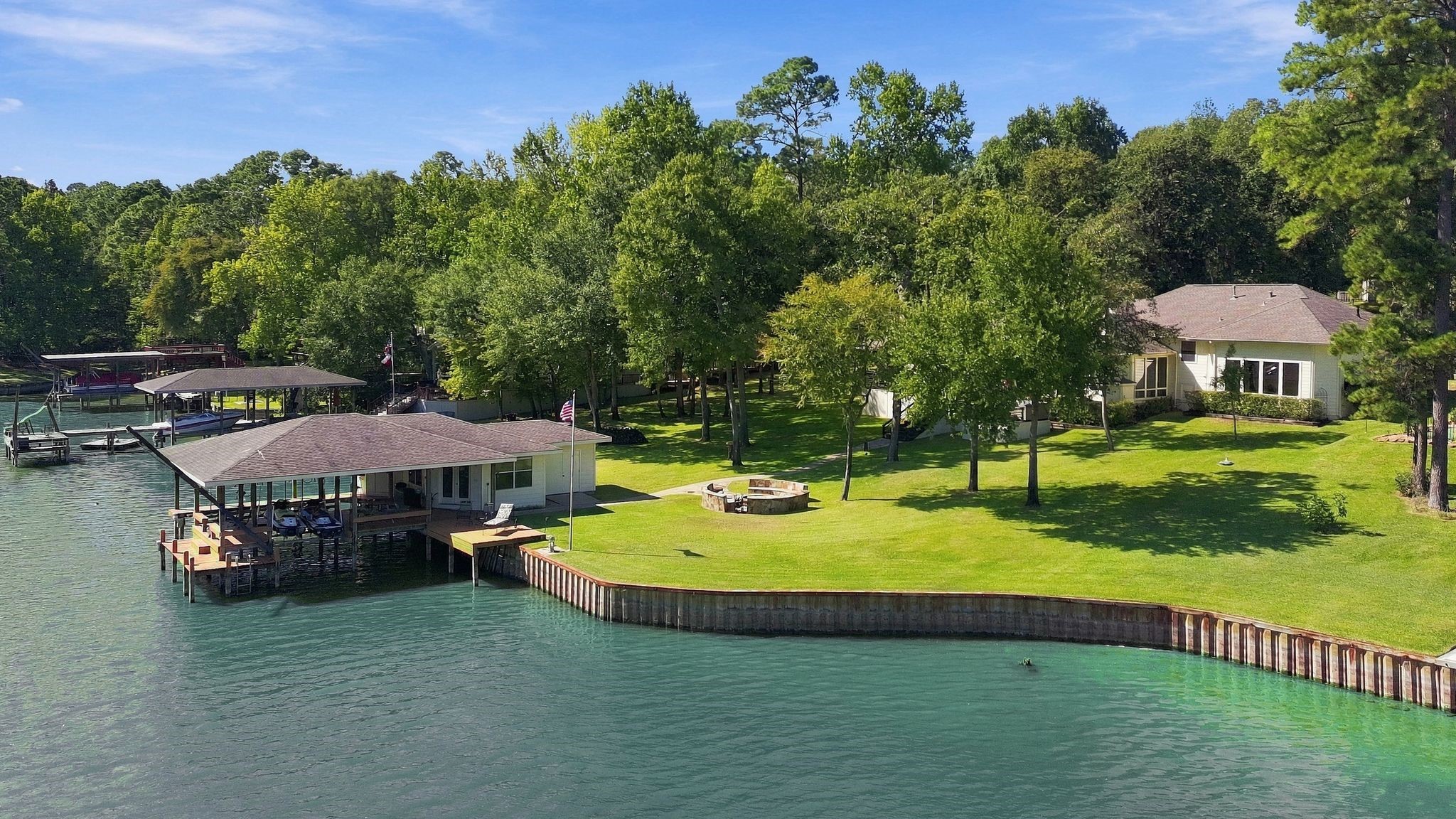 20341 Bay Hill Road Point Blank, TX 77364 - Photo 47 of 50 Lakeside backyard featuring a stone fire pit area, mature trees, and covered boat dock.