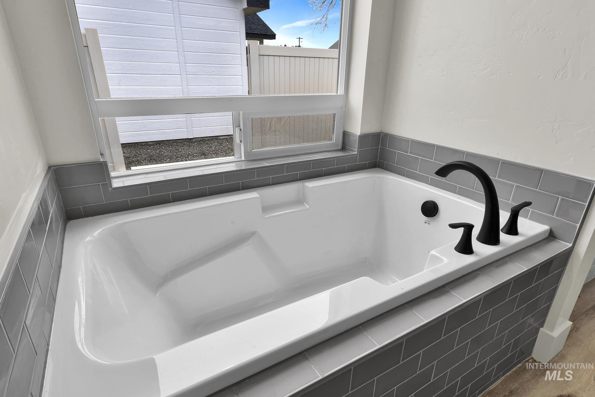 1130 Velvet Loop Wilder, ID 83676 - Photo 22 of 35 White soaking tub featuring matte black fixtures, surrounded by gray subway tile, and a privacy window