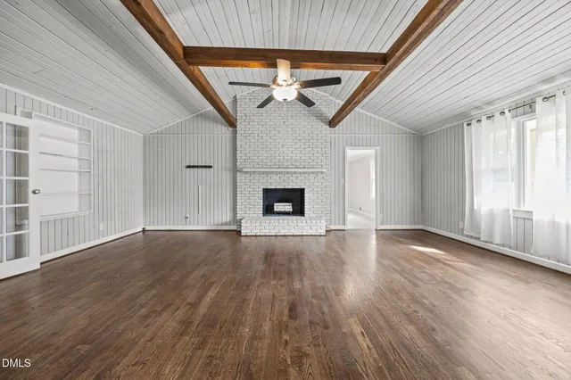 an empty room with wooden floor fireplace and windows