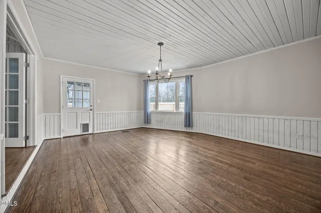 an empty room with wooden floor chandelier and windows