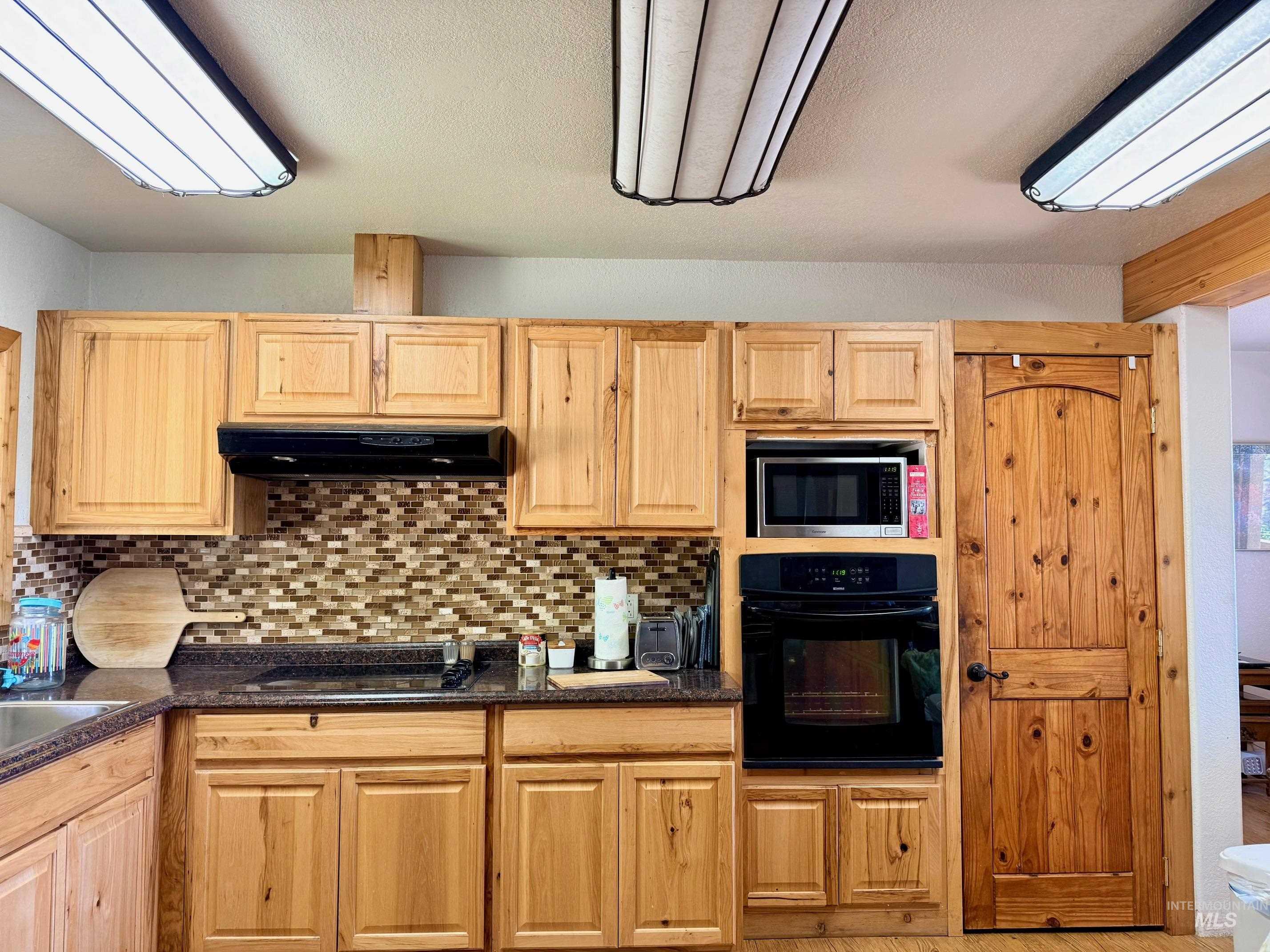 35322 River Road Lenore, ID 83541 - Photo 14 of 42 Kitchen featuring wood cabinetry, dark countertops, a mosaic tile backsplash, built-in microwave, and an integrated oven