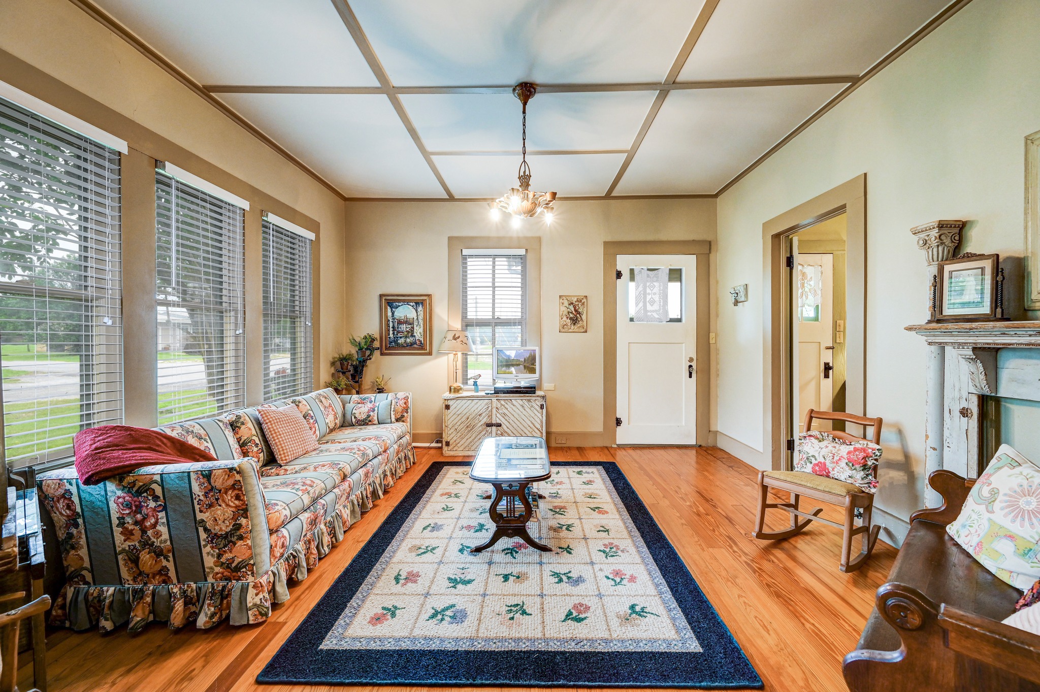 719 Elm Street Blanco, TX 78606 - Photo 9 of 25 Living area featuring hardwood flooring, a coffered ceiling, multiple windows with blinds, a white paneled door, and a decorative fireplace with a mantel