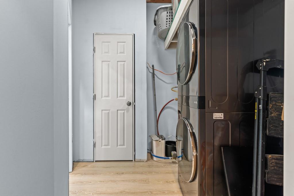 1129 Holly Road Gilmer, TX 75644 - Photo 23 of 31 Laundry area featuring wood-finish flooring, a white paneled door, and a stacked washer and dryer unit
