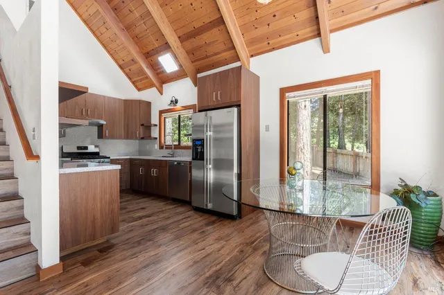 a kitchen with stainless steel appliances granite countertop a refrigerator a sink dishwasher a stove and a dining table with wooden floor