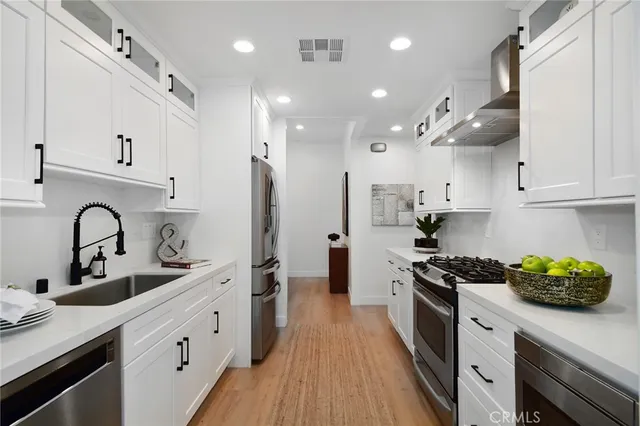 a kitchen with stainless steel appliances granite countertop a sink dishwasher a stove and a refrigerator with wooden floor