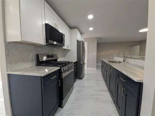 a kitchen with stainless steel appliances granite countertop a sink a stove top oven a refrigerator with grey cabinets