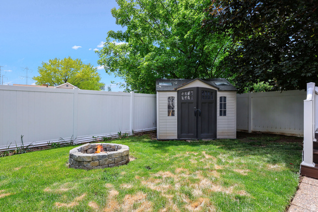 142 East 2675th Street South Clearfield, UT 84015 - Photo 38 of 49 Expansive backyard featuring a stone fire pit, a vinyl privacy fence, and a utility shed with double doors and window accents